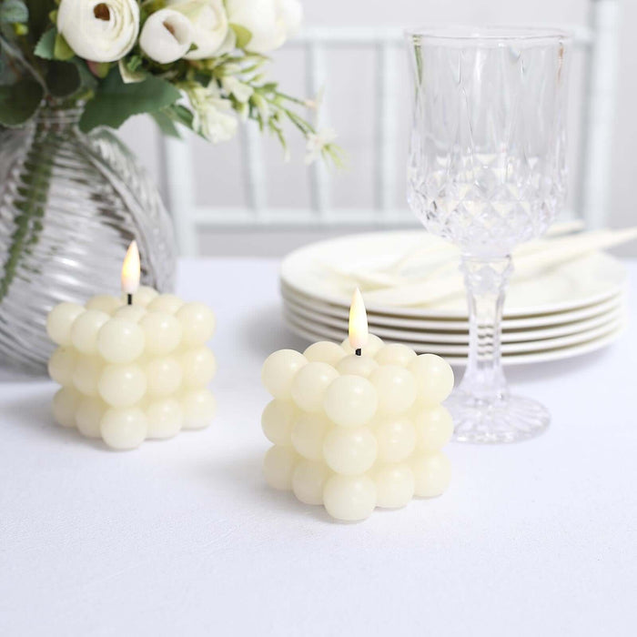 White bubble candles beside a crystal glass and plates on a table.