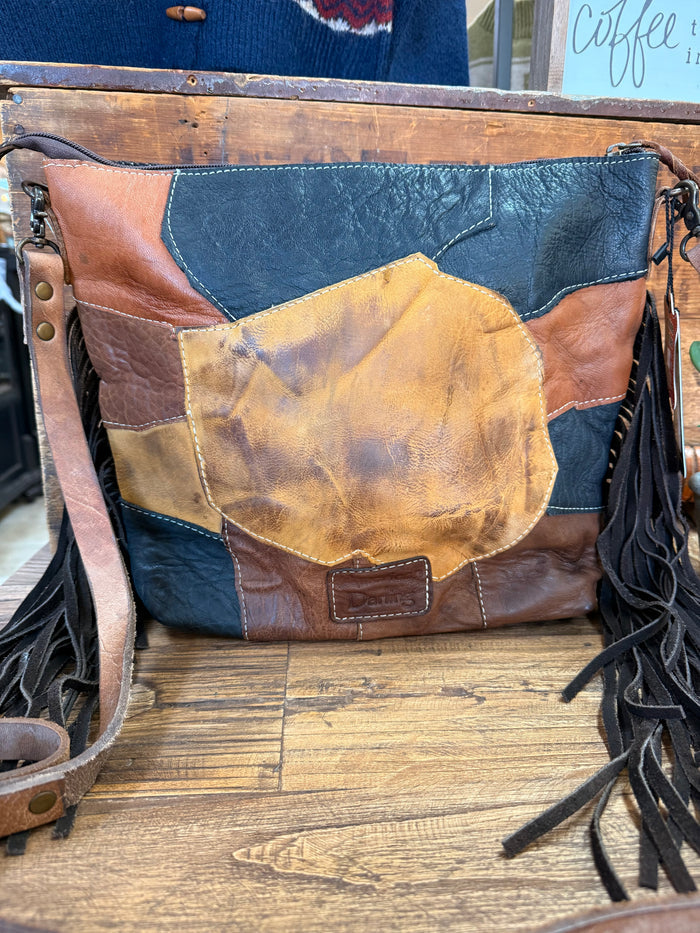 Leather crossbody purse with dark blue and brown panels, gold patch, and fringe tassels
