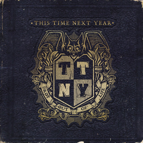 The Drop Out Of Life CD by This Time Next Year features a dark, textured cover with a gold crest displaying TTNY, a bat, and decorative flourishes. The album title appears on a banner below the crest.
