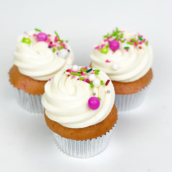 Three cupcakes with white frosting and green and pink sprinkles on top