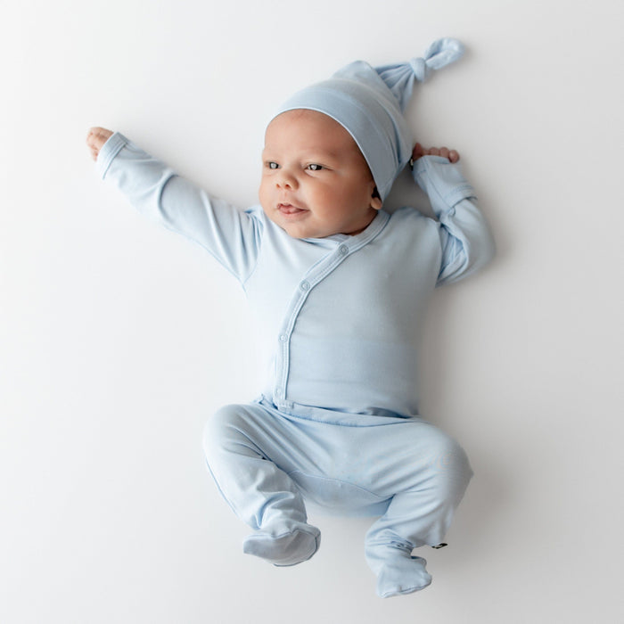 Newborn stretching on a light neutral surface wearing the Take Me Home Set with Cap in Breeze