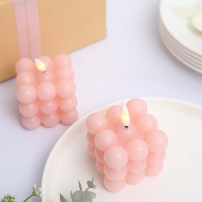 Pink bubble candle with a flickering flame on a white plate.