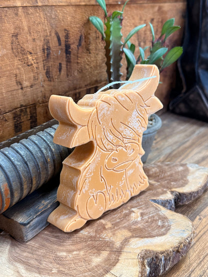 Gold highland cow candle side view with embossed head, curled horns, wick