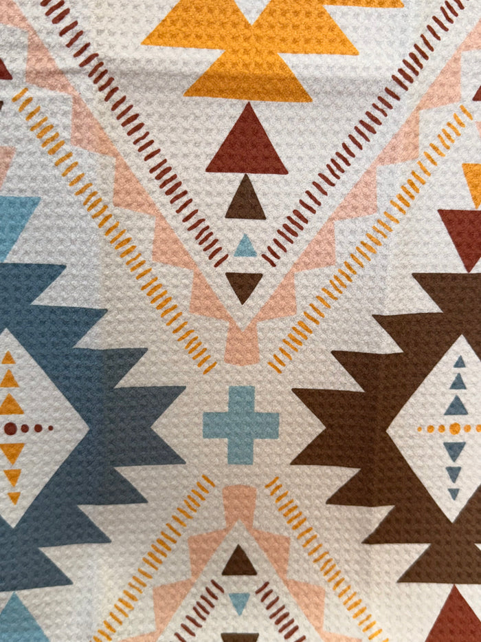 Cream Aztec towel pattern close-up with blue rosette, brown triangles, orange zigzag border, plus sign.