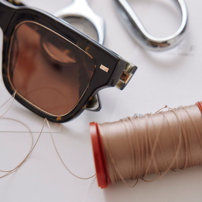 still life of emily in paris x diff eyewear featuring the alfie rectangle sunglasses with a truffle tortoise frame and deep brown lenses detailed view surrounded by designer tools