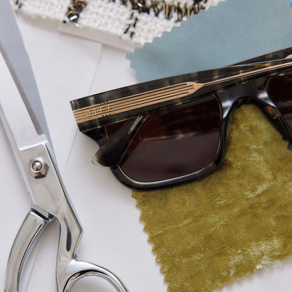 still life of emily in paris x diff eyewear featuring the alfie rectangle sunglasses with a truffle tortoise frame and deep brown lenses detailed view of temple leg surrounded by designer tools