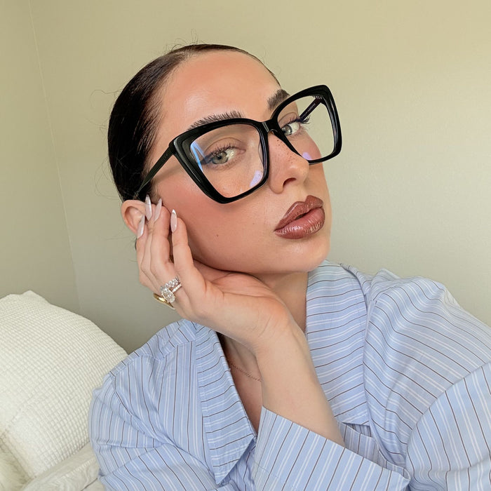lifestyle - emily gordon brunette influencer wearing light blue cotton blouse with oversized black cat eye blue light glasses