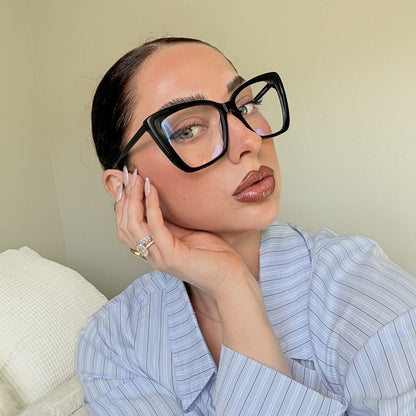 lifestyle - emily gordon brunette influencer wearing light blue cotton blouse with oversized black cat eye blue light glasses
