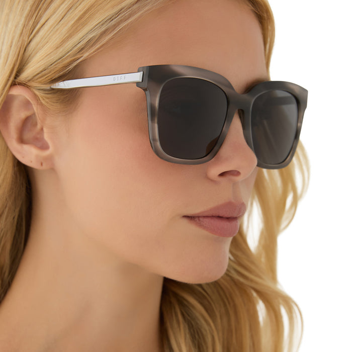 on model - blonde female wearing diff eyewear featuring the bella square sunglasses with a smoke marble frame and grey polarized lenses angled view