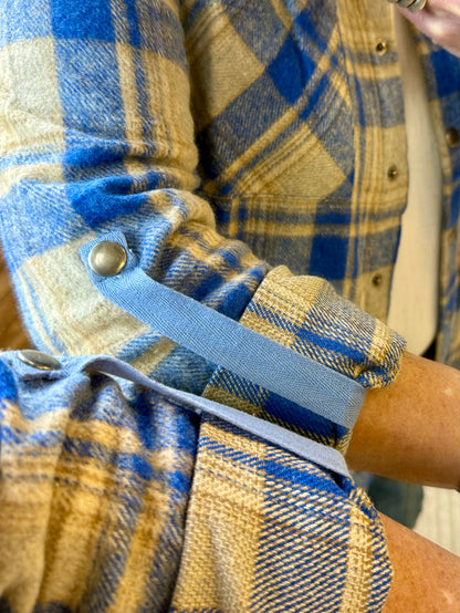 Close-up of blue and tan plaid shacket cuff with button and gathered sleeve