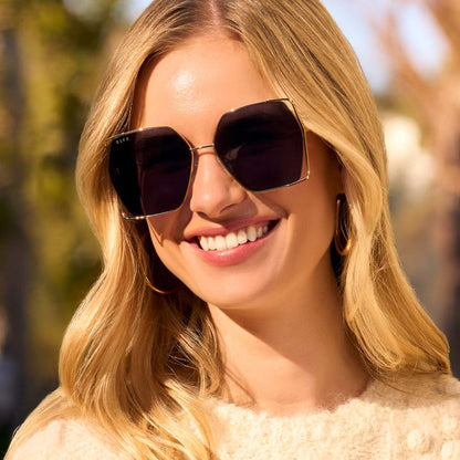 on model - female wearing diff eyewear featuring the donna iv square sunglasses with a gold frame and midnight blue polarized lenses front view