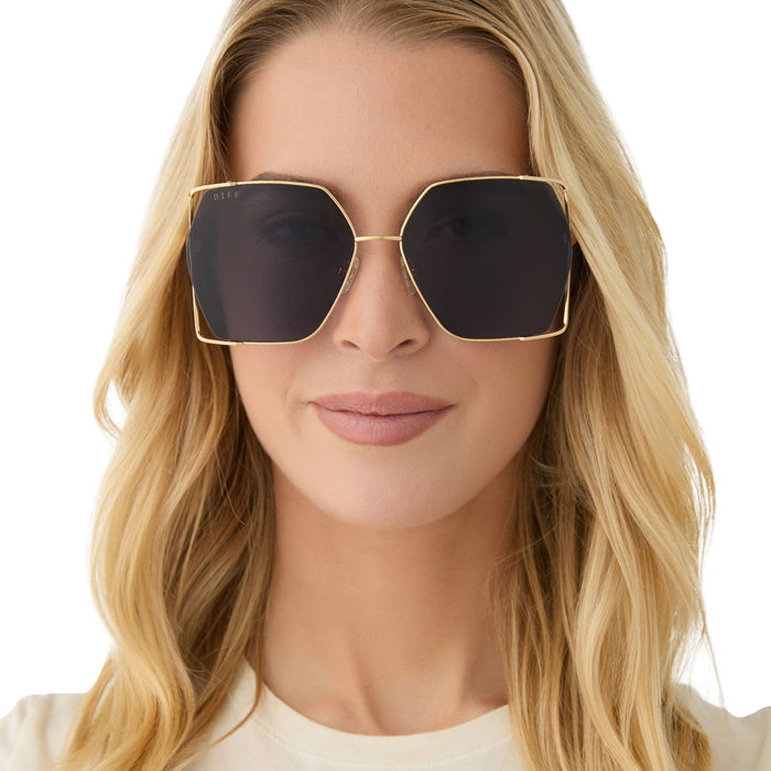 on model - female wearing diff eyewear featuring the donna iv square sunglasses with a gold frame and midnight blue polarized lenses front view