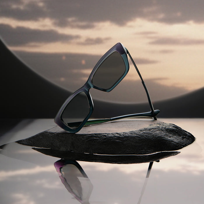 lifestyle - wicked x diff eyewear featuring the elphaba emerald square sunglasses with a black green gradient frame and grey lenses laying on a rock