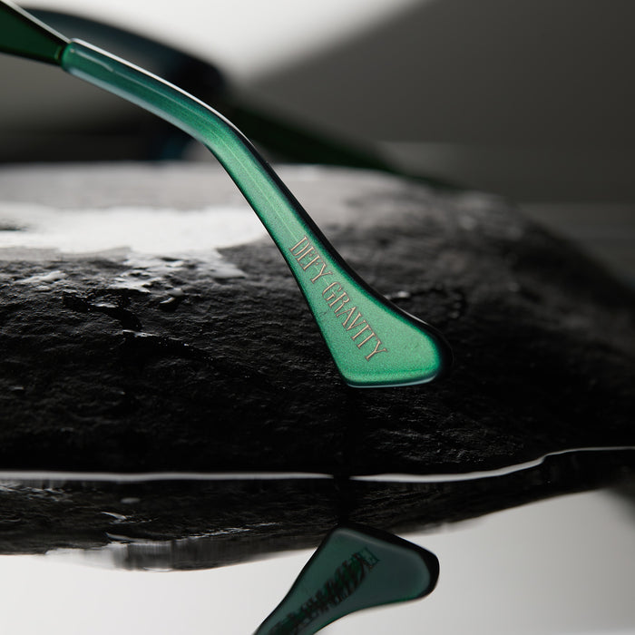 lifestyle - wicked x diff eyewear featuring the elphaba emerald square sunglasses with a black green gradient frame and grey lenses detailed view of temple tip with defy gravity quote