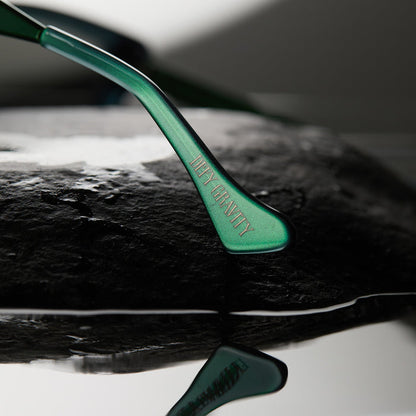 lifestyle - wicked x diff eyewear featuring the elphaba emerald square sunglasses with a black green gradient frame and grey lenses detailed view of temple tip with defy gravity quote