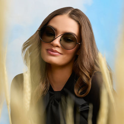 lifestyle - female wearing wicked x diff eyewear featuring the elphaba wire frames round sunglasses with a black frame and green lenses front view