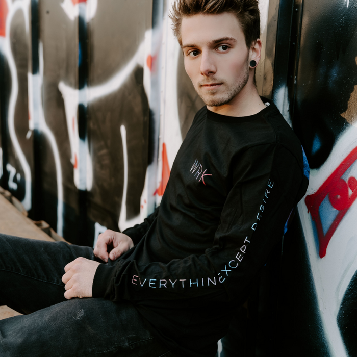 Someone wearing a Black long sleeve shirt with text in the top corner that says WRK in multicolored lettering. On one sleeve, there is similar styled text that says EVERYTHING EXCEPT DESIRE.