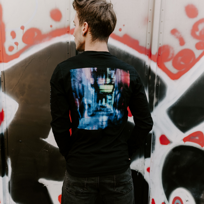 Someone wearing Back of black long sleeve shirt. There is artwork of a long hallway / alley, that is multicolored in the same way as the font