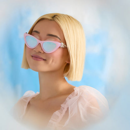 lifestyle - female wearing wicked x diff eyewear featuring the glinda upland for good cat eye sunglasses with a pink frame and pink lenses front view