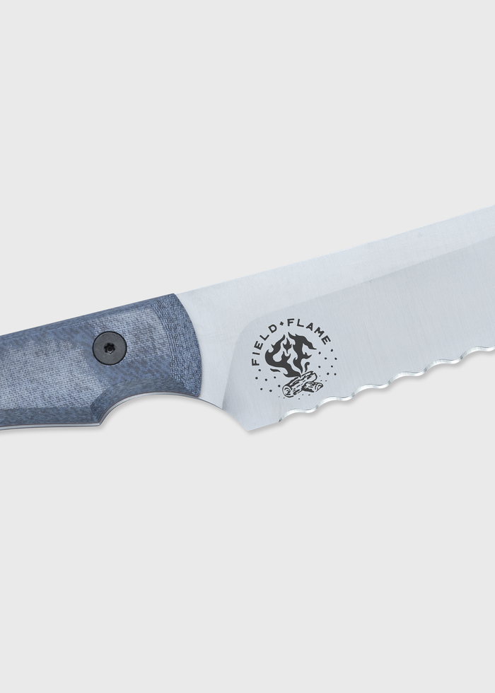 Close-up of a serrated knife blade with a blue handle, featuring the "Field & Flame" logo on a light gray background.