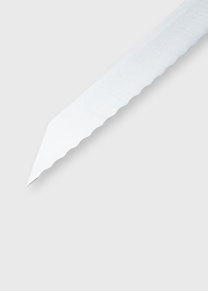 Close-up of a serrated knife blade on a light gray background, showcasing its sharp, jagged edge and metallic sheen.