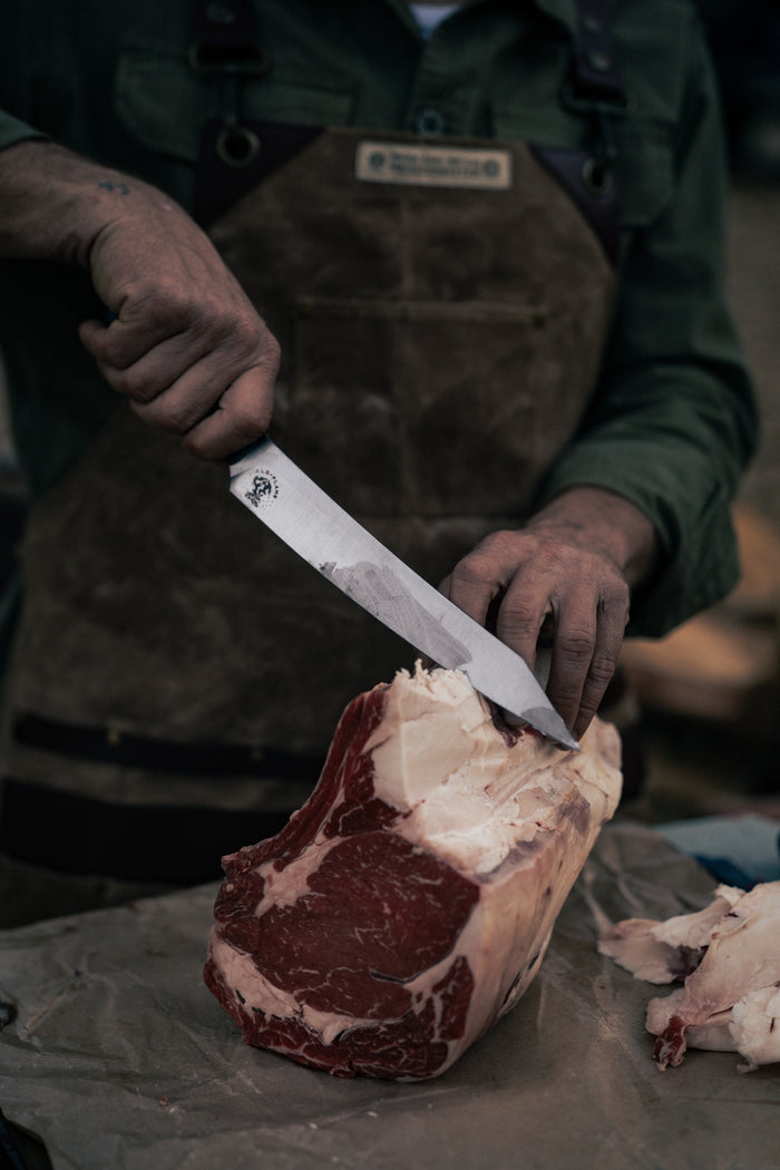 Butcher in apron skillfully slices raw beef with a sharp knife on a wooden table, showcasing precision and expertise in meat cutting.