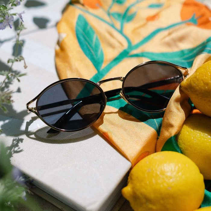 flat lay of jessie james decker diff eyewear limoncello oval sunglasses with a gold frame and grey lenses top view