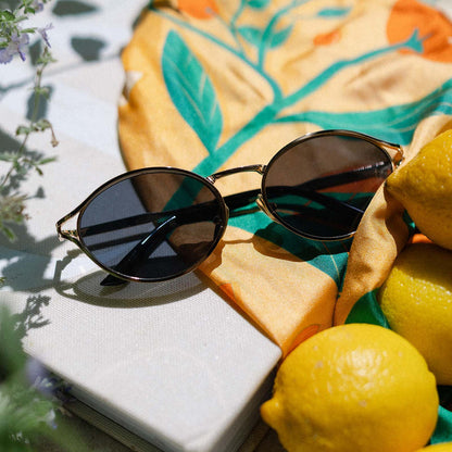 flat lay of jessie james decker diff eyewear limoncello oval sunglasses with a gold frame and grey lenses top view