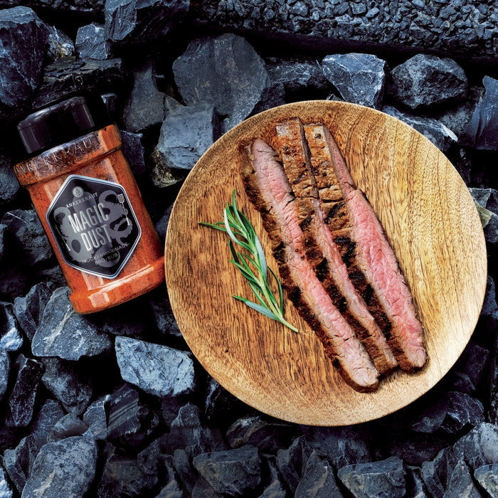 Magic Dust Rub neben einem frisch gegrillten und filetierten Steak auf einem Holzteller.