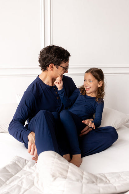 Woman and young girl in matching blue outfits sitting on a white bed.
