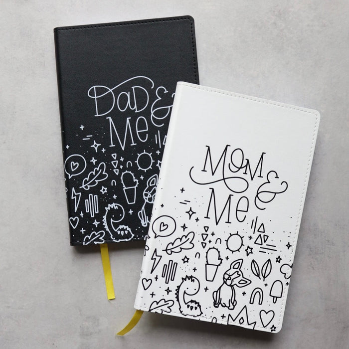 The mom & me journal partially on top of the dad & me journal on a desk