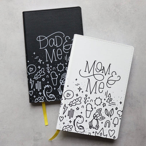 The mom & me journal partially on top of the dad & me journal on a desk