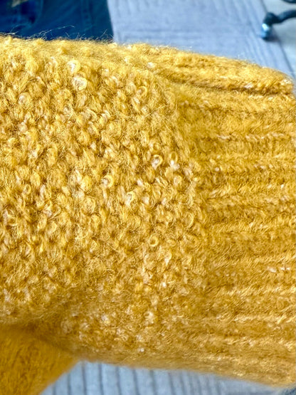 Mustard cable-knit sleeve detail with raised texture along the arm