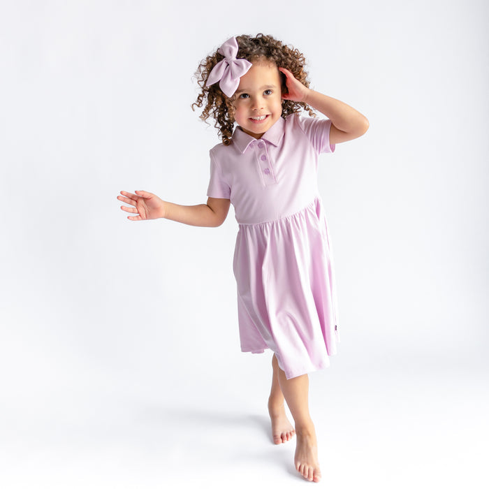 Young girl walking wearing the Polo Dress in Thistle in front of a white background