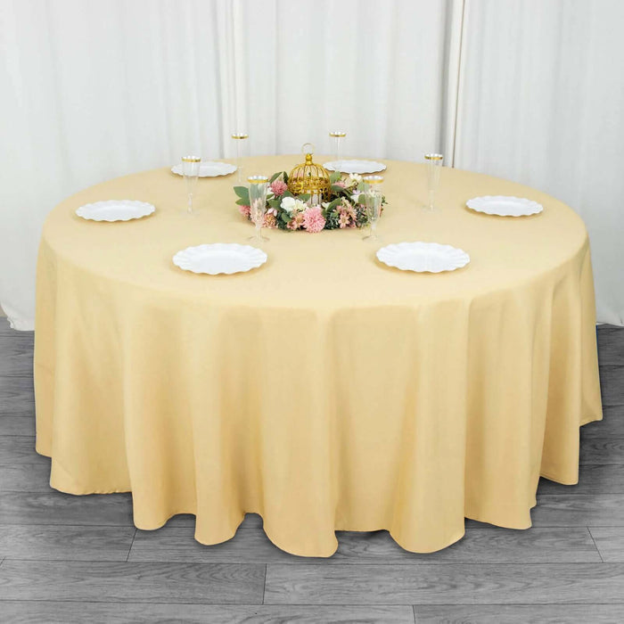 Round yellow tablecloth with elegant floral centerpiece and plates set for dining.