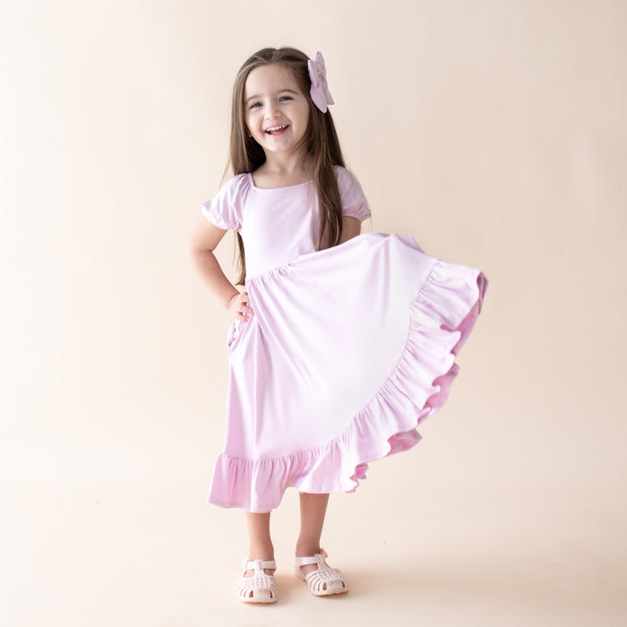Young girl wearing a light purple dress with ruffled skirt on a beige background