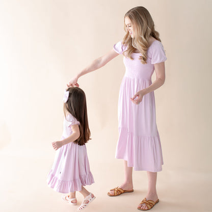 Woman and young girl wearing matching light purple dresses against a beige background
