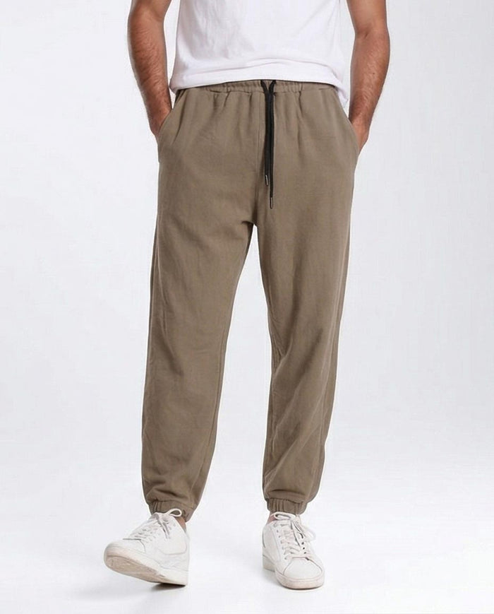 Person wearing beige jogger pants and white sneakers on a white background