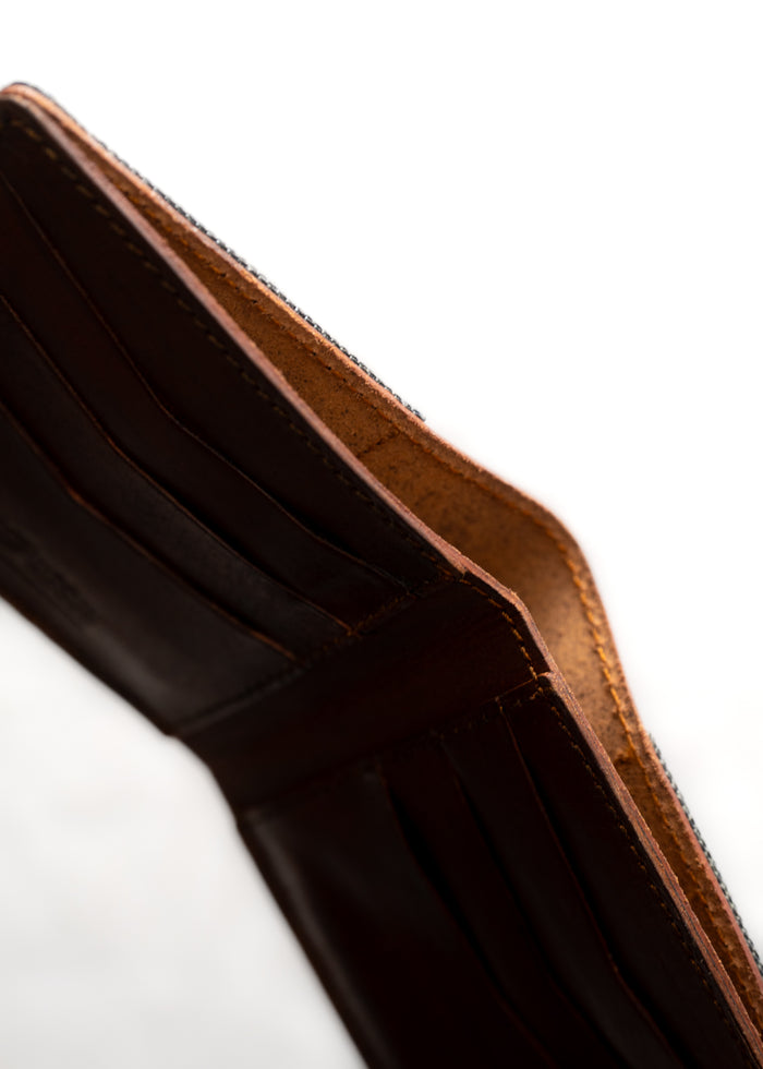 Open brown leather wallet with visible card slots, highlighting craftsmanship and texture against a soft, light background.