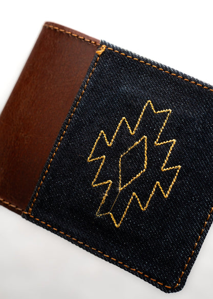 Brown leather wallet with denim patch, featuring a yellow geometric embroidery pattern, creating a stylish, textured design.
