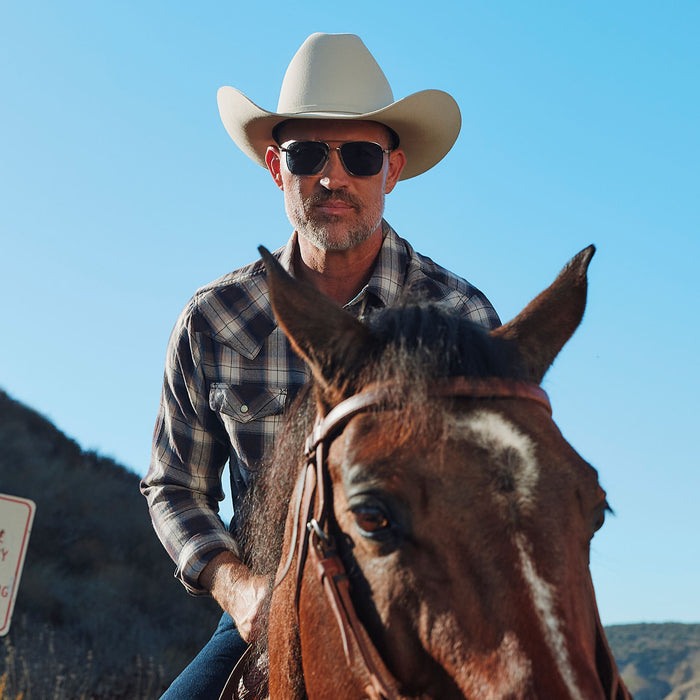 lifestyle - male riding a horse wearing yellowstone x diff eyewear featuring the rip wheeler navigator sunglasses with a silver frame and grey polarized lenses front view