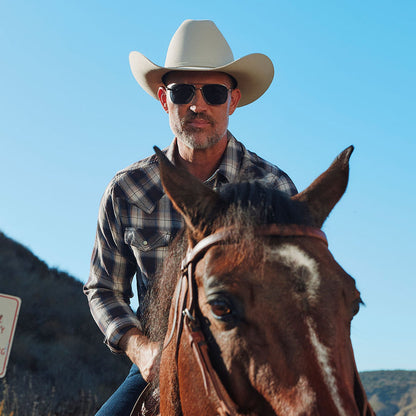 lifestyle - male riding a horse wearing yellowstone x diff eyewear featuring the rip wheeler navigator sunglasses with a silver frame and grey polarized lenses front view