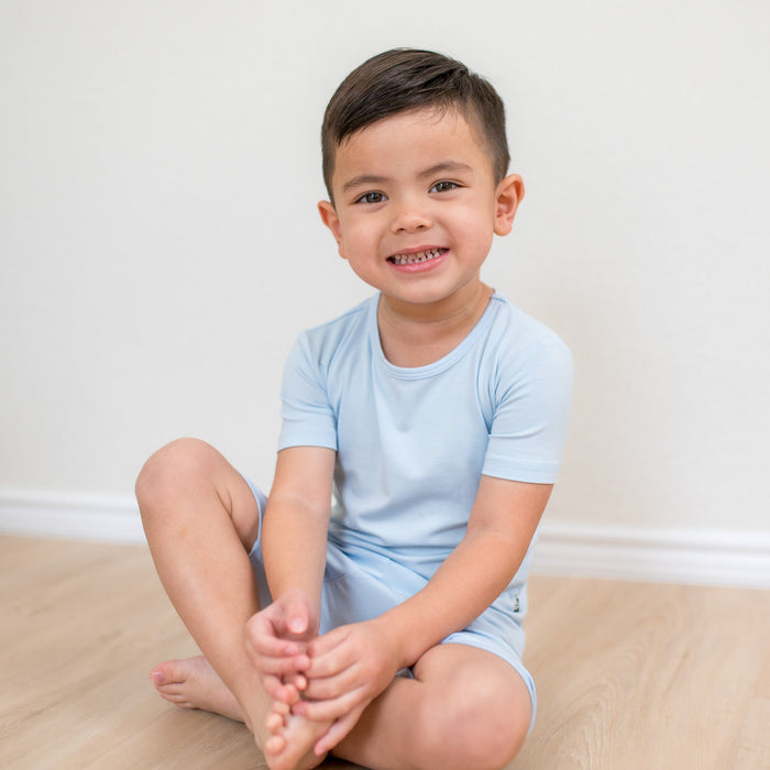 Young boy sitting on a wood grained floor wearing the Short Sleeve Pajamas in Breeze