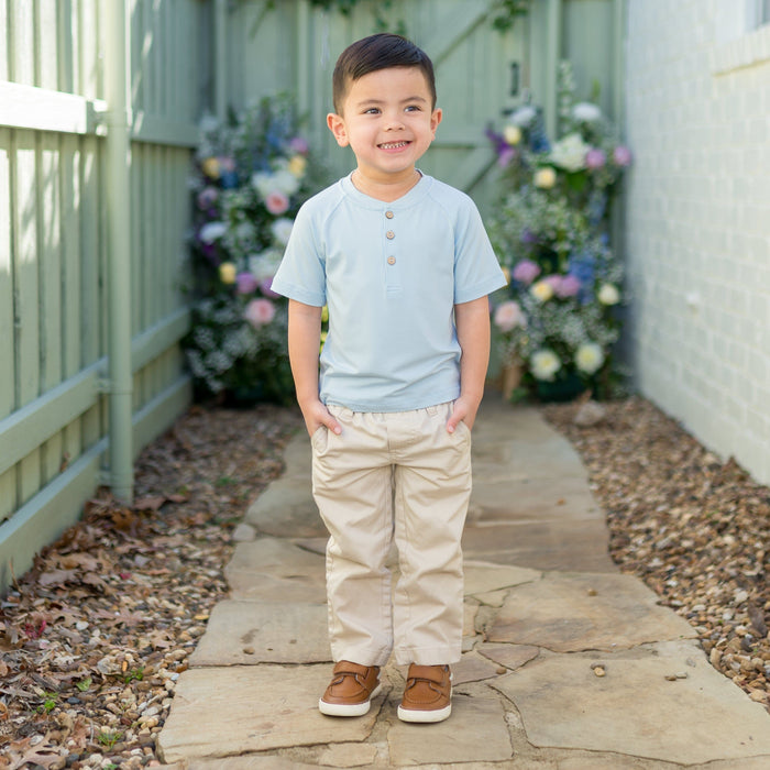 Young boy wearing the Short Sleeve Toddler Henley Tee in Breeze with kakhi colored pants standing on a path