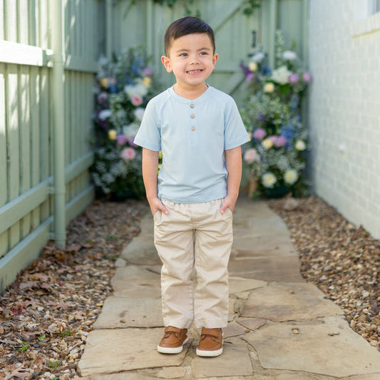 Young boy wearing the Short Sleeve Toddler Henley Tee in Breeze with kakhi colored pants standing on a path