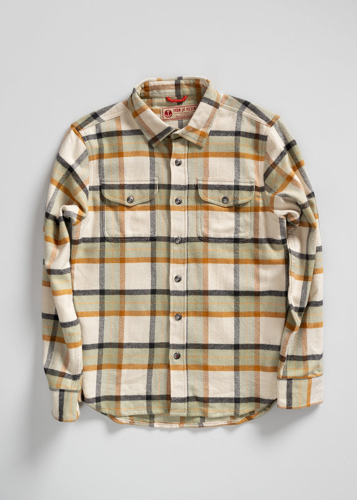 Plaid flannel shirt with beige, orange, and black checks, featuring buttoned front and pockets, laid flat on a white background.