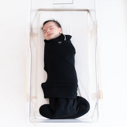 Sleeping baby swaddled in the Sleep Bag Swaddler in Midnight 1.0 laying in a bassinet