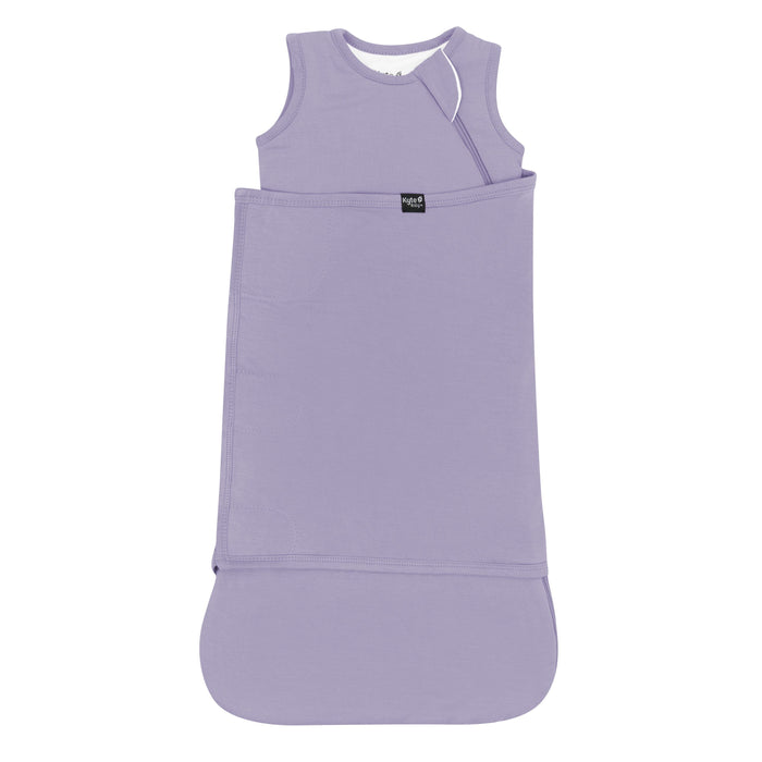 Sleep Bag Swaddler in Taro 1.0 shown swaddled with the black Kyte Baby logo tag visible