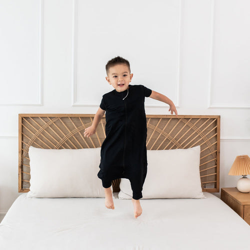 Child model jumping on a bed wearing the Sleep Bag Walker in Midnight 0.5