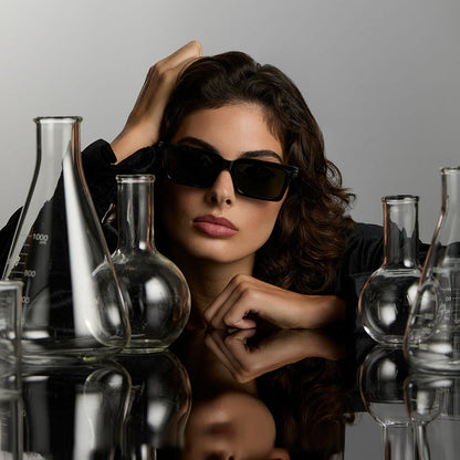 lifestyle - female surrounded by potion flask wearing harry potter x diff eyewear featuring professor snape 2.0 square  sunglasses with a black frame and g15 lenses front view